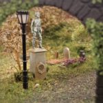 Blick durch Tor auf Modellbau-Statue in einem detailgetreuen Miniaturfriedhof