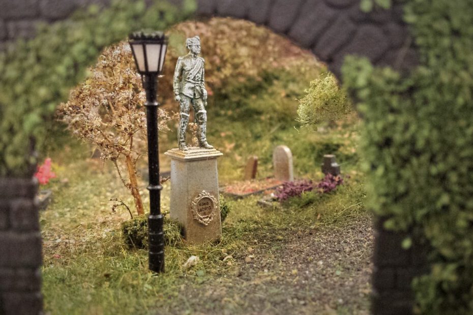 Blick durch Tor auf Modellbau-Statue in einem detailgetreuen Miniaturfriedhof
